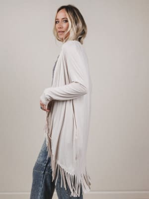 Woman wearing a white cardigan with fringe details against a plain background