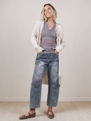 Woman wearing a gray top, white cardigan, and blue jeans with a floral pattern.