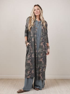 Woman wearing a long camouflage cardigan over a blue dress against a plain background