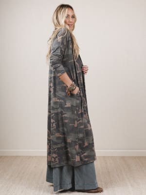 Woman wearing a long camouflage dress against a plain background