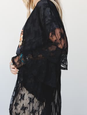 A close torso shot of a black lace kimono layered over a floral top and a sheer pleated skirt, styled with stacked turquoise and gemstone bracelets and rings — moody, effortless, and very much the outfit you'd wear when you want to feel a little myst