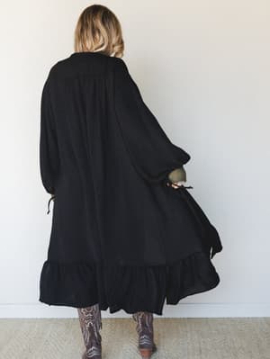 A flowy black duster kimono photographed from behind, styled with embroidered brown cowboy boots — the kind of outfit that feels like it has a whole personality before you even turn around.