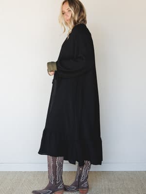 A long black duster kimono with a relaxed, flowing silhouette is styled over an olive ribbed layer and paired with brown embroidered cowboy boots — effortlessly moody with a western-boho edge.