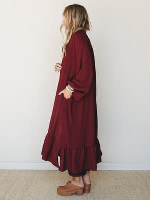 A long wine-colored duster kimono styled with dark denim and wooden clogs — the kind of effortless layering piece that makes a Tuesday feel intentional.