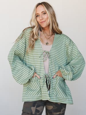 A relaxed, oversized gingham cardigan in sage green styled open over a blush tank with camo pants — the kind of effortless layering that looks like you meant to do it.