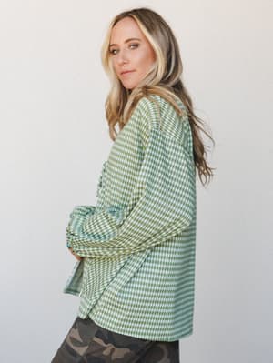 A relaxed side-profile shot of a model in an oversized green gingham long-sleeve top paired with camo leggings — the kind of effortless, pattern-mixing look that feels intentional without trying too hard.