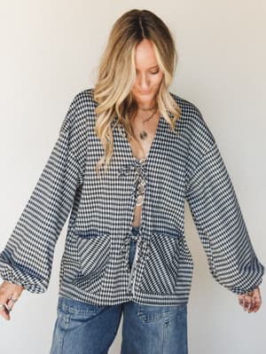 A relaxed gingham cardigan with a front tie closure and billowy sleeves, styled open over a lace bralette and wide-leg jeans — the kind of layered, lived-in look that feels effortless without trying.