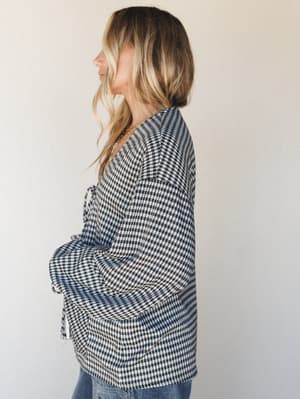 A side-profile shot of a model in a relaxed gingham top with wide sleeves and a wrap-style tie detail — the kind of top that looks intentional with jeans and a gold necklace on a slow Saturday.