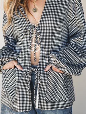 A gingham tie-front cardigan in black and white worn open over a lace bralette and denim, styled with a gold pendant necklace — casual and a little undone in the best way.