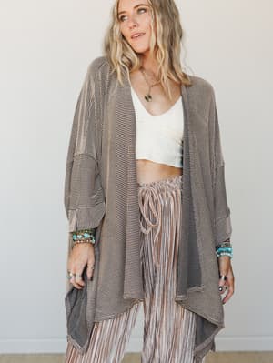 A relaxed, effortlessly layered look featuring an oversized ribbed duster cardigan in camel tones styled over a white cropped top and striped drawstring pants, finished with turquoise and silver stacked jewelry for that lived-in boho feel.