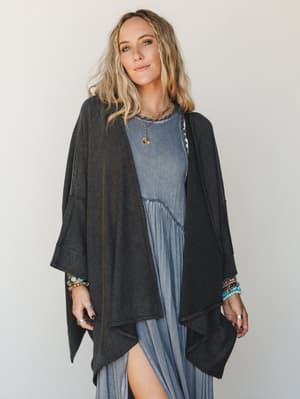 A relaxed, layered look featuring an oversized ribbed duster cardigan in charcoal draped over a washed blue maxi dress — the kind of outfit that feels equally at home on a slow morning or a long weekend.