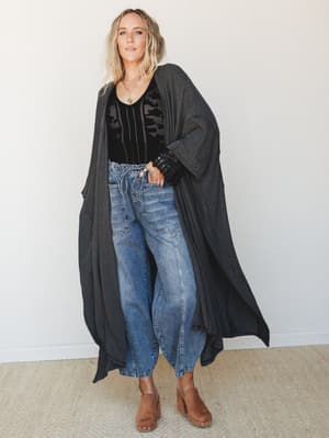 A flowy, floor-length striped duster kimono in charcoal layered over a black crochet tank and relaxed high-waist jeans — the kind of effortless outfit that looks like it took no time but clearly did.