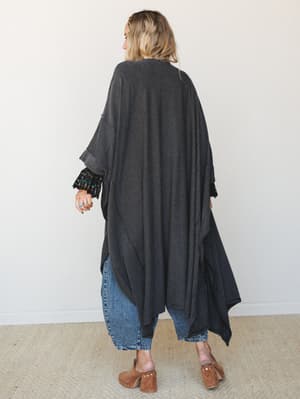 Shot from behind, a model wears a floor-grazing striped duster kimono in charcoal over straight-leg jeans and cognac wood clogs — the kind of effortless layering piece that makes a whole outfit feel intentional.
