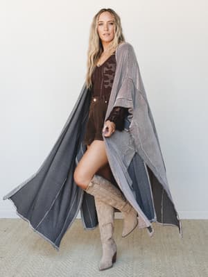 A flowy, floor-length duster kimono in a two-tone stripe is styled over a chocolate brown lace bodysuit and mini shorts with over-the-knee suede cowboy boots — the kind of outfit that makes a casual errand feel like a whole moment.