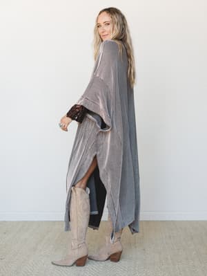 A long, flowing duster kimono in a fine stripe knit layers over black skinny pants and tan cowboy boots — the kind of effortless outfit that looks like you just threw it on and somehow got it exactly right.