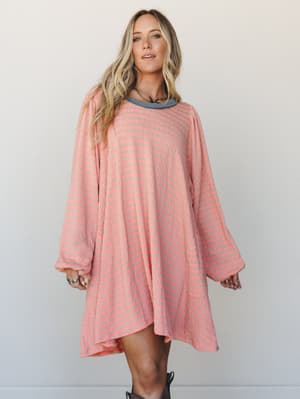 An oversized striped knit mini dress in warm peach and sage, styled with brown cowboy boots and layered necklaces — the kind of effortless outfit that looks like you tried just enough.