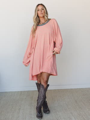 An oversized striped knit mini dress in warm peach and slate blue paired with dark brown cowboy boots — the kind of effortless outfit that looks like you tried just the right amount.