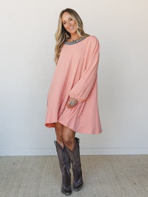 A relaxed mini dress in coral-peach and sage stripe worn with tall dark cowboy boots — the kind of outfit that feels effortless but clearly thought through.