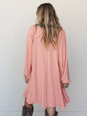 Shot from the back, this flowy striped mini dress in coral pink and warm taupe pairs effortlessly with brown cowboy boots — easy, expressive, and the kind of outfit that looks like it came together without trying.