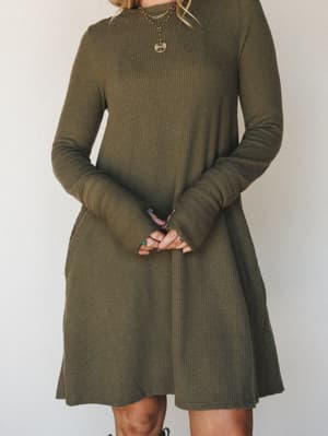 A ribbed knit mini dress in dusty olive worn with layered gold chain necklaces — the kind of dress that works just as hard on a coffee run as it does on a casual dinner night.