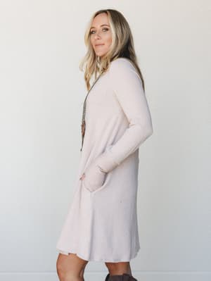 A relaxed ribbed knit midi dress in a soft oat tone, styled with a long pendant necklace and ankle boots — the kind of effortless outfit that looks like you tried just the right amount.