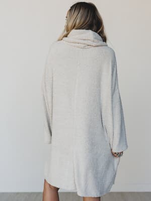 Person wearing a light gray sweater dress against a plain background
