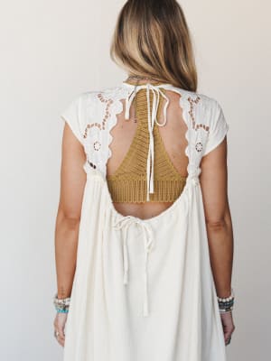 Shot from behind, this cream dress does the quiet work of being unforgettable — eyelet lace shoulders, a deep open back with tie closure, and a mustard crochet bralette peeking through, layered with turquoise and stone bracelets that feel like souven