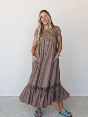 A flowy mocha maxi dress with crochet trim details at the chest and hem ruffle, styled with turquoise sandals and layered boho jewelry — the kind of outfit that feels effortless but clearly thought through.