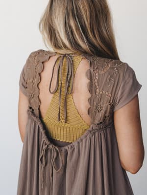 A close back-detail shot of a mocha dress with intricate floral embroidery and an open back, revealing a mustard yellow lace bralette underneath — the kind of layered, effortless detail that makes a dress worth turning around for.