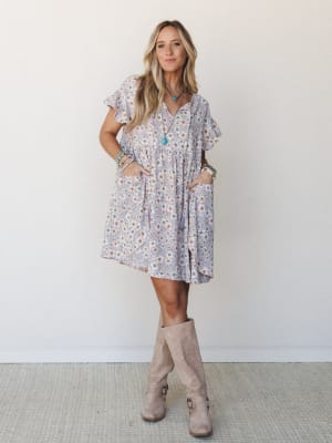 A flowy lavender floral mini dress with flutter sleeves and front pockets, styled with tall suede boots and turquoise jewelry for an easy boho-casual look.