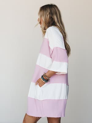 A relaxed mini dress in wide orchid pink and ivory stripes, styled with a stack of mixed bracelets — the kind of effortless piece that looks just as good at brunch as it does barefoot on a patio.