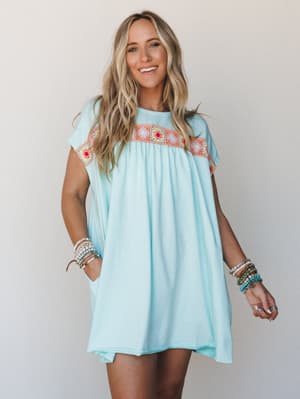 A breezy mint mini dress with a colorful granny square crochet panel across the chest, styled with stacks of beaded bracelets — the kind of dress that earns compliments at the farmers market and doubles as a beach cover-up without trying.