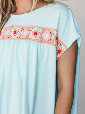 A close-up of a light mint casual dress with a cheerful granny square crochet panel across the chest — the kind of piece that feels like a summer afternoon in wearable form.