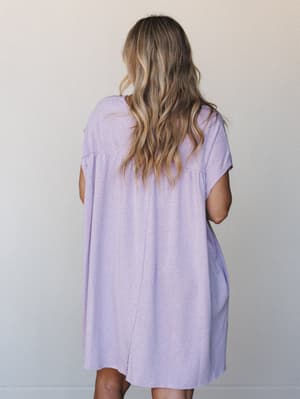 A soft lavender t-shirt dress photographed from the back, showing its relaxed babydoll silhouette with cap sleeves and a center back seam — the kind of effortless everyday dress that looks like you meant to be this comfortable.