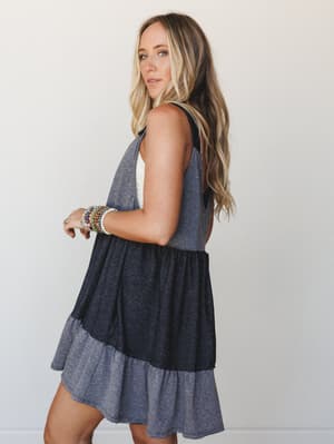 A tiered colorblock babydoll mini dress shot from a three-quarter back angle — the kind of effortless piece that looks just as good at brunch as it does on a last-minute road trip.