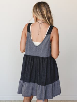 Shot from the back, this color-blocked tiered babydoll dress in heathered grey and charcoal layers has a relaxed, effortless feel — styled with a lariat chain necklace that shows off the low open back.