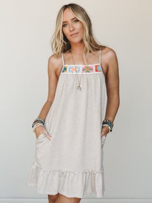A relaxed mini dress in oatmeal heathered knit gets its personality from a colorful granny square crochet panel at the chest — the kind of dress that looks like it belongs at a farmers market or a beach town lunch, styled with stacked boho bracelets