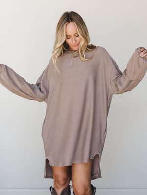 An oversized mini sweater dress in warm acorn tones styled with dark cowboy boots — the kind of effortless fall outfit that looks like you tried just enough.