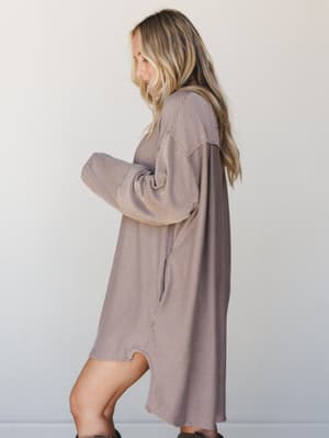 A relaxed, oversized sweater mini dress in a warm mocha stripe worn from the side — the kind of effortless piece that looks like you tried just enough.