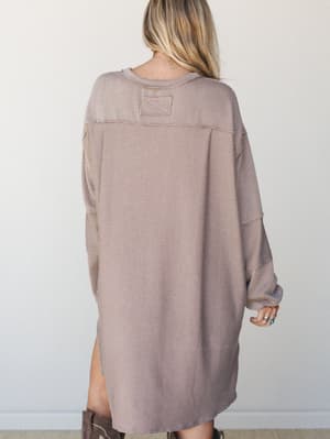 Shot from the back, this oversized thermal mini dress in warm acorn tones has the kind of effortless, thrown-on energy that makes it feel like a weekend uniform — styled with stacked rings and tall brown boots.