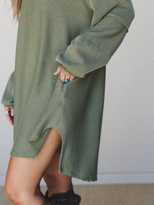 A close-cropped detail shot of an oversized olive striped mini dress with a relaxed, lived-in feel — the model's turquoise and silver rings tucked into a side pocket say everything about the girl wearing it.