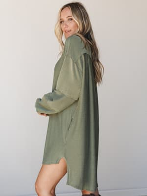 A slouchy, oversized mini dress in army green ribbed knit, shot in profile against a clean studio wall — the kind of piece that looks equally at home on a coffee run or a casual dinner out.