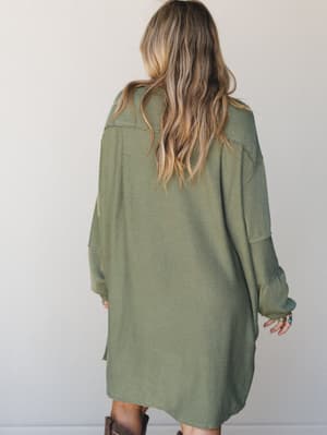 Shot from behind, a model in an oversized army green ribbed mini dress pairs it with brown leather boots — the kind of effortless, lived-in look that feels equally at home on a coffee run or a weekend road trip.