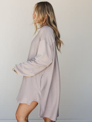A relaxed, oversized mini dress in a soft striped knit photographed from the side — the kind of piece that looks like it was made for slow mornings and staying in it all day anyway.