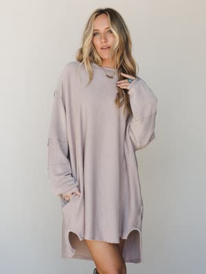 An oversized ribbed knit mini dress in a warm oat-and-mauve stripe, styled with stacked turquoise rings and a delicate gold necklace — the kind of dress that looks like you tried just enough.