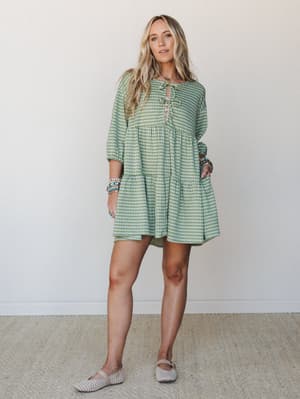 A breezy gingham mini dress in sage green styled with stacked boho bracelets and woven flats — the kind of dress that feels as good as it looks on a warm afternoon.