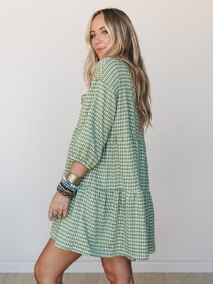 A breezy green gingham mini dress with a tiered skirt and three-quarter sleeves, styled with a stack of boho bracelets — the kind of dress that makes a grocery run feel like a picnic.