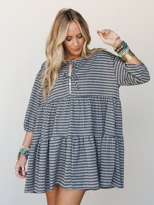 A tiered mini dress in a classic black-and-white gingham styled with stacks of boho bracelets — relaxed and a little whimsical, like something you'd wear to a fall farmers market and somehow look effortlessly put-together.