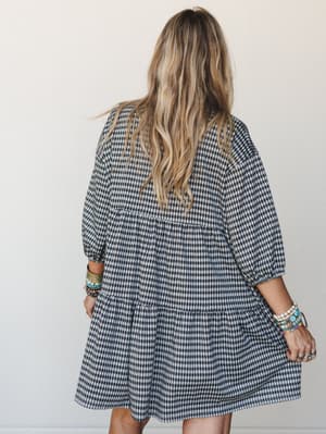 Shot from behind, a model in a gingham mini dress stacked with colorful boho bracelets — the kind of effortless, lived-in look that makes you want to copy the whole outfit.