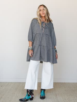 A gingham tiered mini dress styled over wide-leg white jeans with embroidered teal cowboy boots and stacked bracelets — that mix of playful pattern and Western edge that just works.